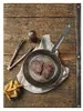 A rustic wooden table setting with a frying pan containing two steaks, a side of french fries, and cooking utensils. Náhľad obrázku produktu