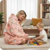 A woman wearing a pink hoodie blanket with a bunny pattern sits on the floor with a young child, playing with wooden blocks. Náhled obrázku produktu