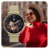 A woman wearing a red sweater and a hat, smiling and touching her face, with a smartwatch in the foreground. Podgląd zdjęcia produktu