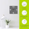 A modern gray wall clock with colorful hour markers is displayed on a light gray wall, next to a white desk lamp and a potted plant. The right side of the image features green marketing panels with text and icons. Produktbild-Vorschau