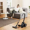 A woman relaxes on a sofa while a vacuum cleaner is in the foreground. Produktbild-Vorschau