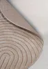 A close-up view of a round rug with a curved line pattern, partially rolled up. Anteprima dell’immagine prodotto