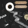 A roll of hemming tape with pins, a measuring tape, scissors, and an alarm clock laid out on a black fabric. Náhled obrázku produktu