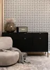 A modern living room scene featuring a black sideboard with fluted doors, a decorative vase with dried flowers, a Marshall speaker, and a textured armchair with a throw blanket. Produktbild-Vorschau