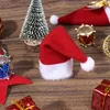 A collection of miniature Christmas decorations, including a Santa hat, a small Christmas tree, and a miniature drum, arranged on a wooden surface. Náhled obrázku produktu