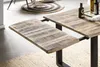 A close-up view of a wooden dining table with an extension leaf pulled out, showing the texture of the wood and the metal legs. Produktbild-Vorschau