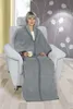 A woman sits in a chair wrapped in a grey blanket, holding a mug. Náhled obrázku produktu
