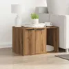 A wooden side table with two doors and an open compartment next to a sofa. A lamp, books, and a plant are on top of the table. Anteprima dell’immagine prodotto
