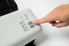 A hand is pressing a button on a document scanner. Voir les images du produit
