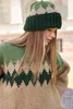 A woman wearing a knitted hat and sweater with a geometric pattern. Produktbild-Vorschau
