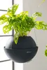 A hanging planter with a plant inside, suspended by wires. Náhľad obrázku produktu