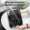 Schwarze Haarverlängerung, die unter einem silbernen Wasserhahn in einem weißen Waschbecken ausgespült wird, von den Händen einer Person gehalten Náhľad obrázku produktu