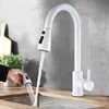 A white kitchen faucet with a pull-out spray head is shown in use over a stainless steel sink. A hand is holding the spray head, demonstrating its functionality. Náhľad obrázku produktu