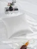 A white silk pillowcase is laid out on a white satin sheet, with a magazine, a small vase of flowers, and a bottle of liquor with a pearl necklace nearby. Podgląd zdjęcia produktu