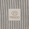 A close-up view of a beige label with a teddy bear logo and the brand name 'MISIOO' on a textured gray background. Produktbild-Vorschau