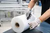 A person wearing gloves is cutting a large roll of clear plastic film with a utility knife. Anteprima dell’immagine prodotto