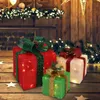 Three illuminated Christmas gift boxes with bows and pinecones are arranged on a wooden surface, with a blurred background of Christmas lights and greenery. Podgląd zdjęcia produktu