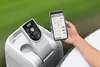 A person is holding a smartphone and controlling a white hot tub with a digital display. Produktbild-Vorschau