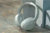 A pair of white over-ear headphones rests on a wooden surface, leaning against a light gray concrete block. Voir les images du produit