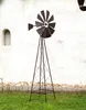 A metal windmill garden stake stands on a grassy lawn in front of a white wall with a small arched niche. Anteprima dell’immagine prodotto