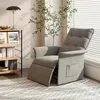 A light gray recliner chair is shown in a well-lit room with natural light coming from a window with blinds. A bookshelf with books and decorative items is to the left, and a plant is behind the chair. A patterned rug is on the floor. Voir les images du produit