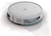 A white robot vacuum cleaner is shown on a white surface, with dirt being picked up. Náhľad obrázku produktu