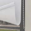 A close-up view of a white roller blind partially unrolled, showing its mechanism and the view through the window. Produktbild-Vorschau