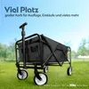 A black foldable wagon is shown outdoors on a grassy field with a blue sky in the background. Produktbild-Vorschau