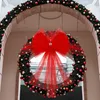 A large, festive Christmas wreath decorated with red and gold ornaments and a big red bow, hanging under an arched entryway. Náhled obrázku produktu