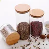 Three glass storage jars with bamboo lids filled with different types of beans and grains, scattered on a white surface. Produktbild-Vorschau