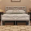 A white metal bed frame with a decorative headboard and footboard, set up in a bedroom with bedside tables and a rug. Produktbild-Vorschau