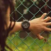 A person's arm with a watch is resting on a green chain-link fence. Podgląd zdjęcia produktu