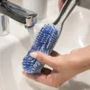 A hand is rinsing a blue brush under a faucet in a sink. Náhled obrázku produktu