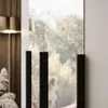 A close-up view of a wardrobe with black handles, seen through a window with trees outside. Produktbild-Vorschau