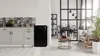 A black mini-refrigerator is shown next to a kitchen counter on the left, and a dining area with a table and chairs is visible on the right. Voir les images du produit