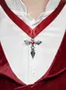 A close-up of a person wearing a white shirt and a red velvet costume, with a silver cross pendant on a red ribbon around their neck. Produktbild-Vorschau
