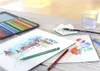 A watercolor painting setup with colored pencils, brushes, water, and sketches on a wooden table. Podgląd zdjęcia produktu