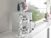 A white controller stand holding a Nintendo Switch controller and two PlayStation controllers, with a white console and TV in the background. Produktbild-Vorschau
