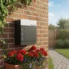 A modern mailbox with a package compartment mounted on a brick wall, with flowers in a planter below and a garden path in the background. Produktbild-Vorschau