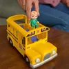 A hand is placing a CoComelon JJ doll into a yellow toy school bus. Voir les images du produit