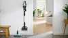 A cordless vacuum cleaner is mounted on a wall in a hallway, with a floor cleaning attachment and pads on the floor. Produktbild-Vorschau