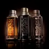 Three bottles of Hugo Boss The Scent for Him perfume are displayed against a dark, gradient background. Náhľad obrázku produktu