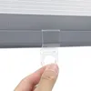 A close-up of a hand holding a clear plastic clip attached to a gray roller blind. Produktbild-Vorschau