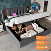 A bed with its storage compartment open, showing various items inside. The bed has a padded headboard with built-in shelves and a glowing light. Produktbild-Vorschau