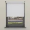 A white roller blind is shown covering most of a window, with a view of a street and trees visible through the lower part of the window. Produktbild-Vorschau