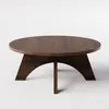 A round, dark brown wooden coffee table with a unique, curved leg design, shown against a plain white background. Produktbild-Vorschau