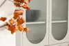 A close-up of a beige cabinet with fluted glass doors and dried leaves in the foreground. Voir les images du produit