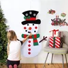 A young girl is decorating a large felt snowman hanging on a wall, with Christmas decorations in the background. Náhľad obrázku produktu