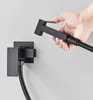 A hand holding a black bidet sprayer over a wall-mounted holder. Náhľad obrázku produktu