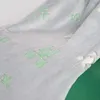 A close-up view of a soft, gray blanket with a repeating pattern of green pixelated shapes, possibly representing a Minecraft Creeper. The blanket is draped over a green surface. Podgląd zdjęcia produktu